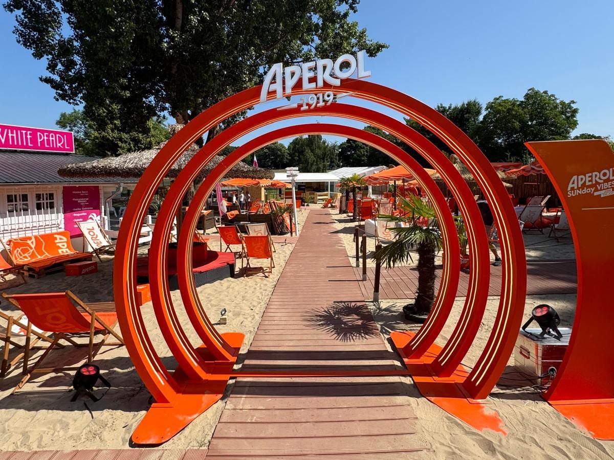 Orangefarbene Eingangsbögen und Liegestühle auf einem Strandgelände, aufgebaut für einen Markenauftritt